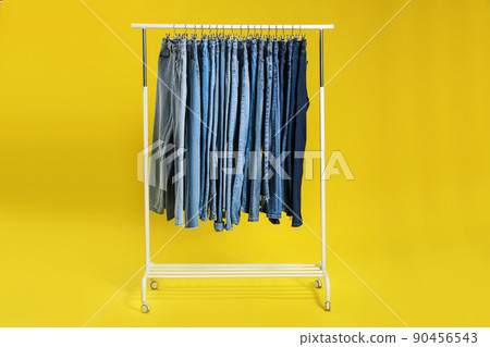 Rack with different jeans on yellow background 90456543