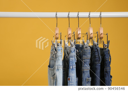 Rack with different jeans on yellow background Rack with different jeans on yellow background 90456546
