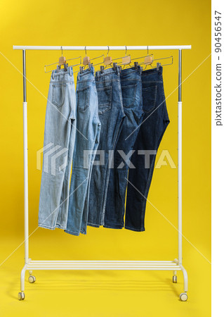 Rack with different jeans on yellow background Rack with different jeans on yellow background 90456547