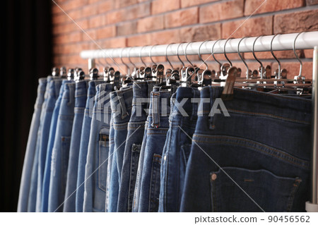 Rack with stylish jeans near brick wall, closeup Rack with stylish jeans near brick wall, closeup 90456562