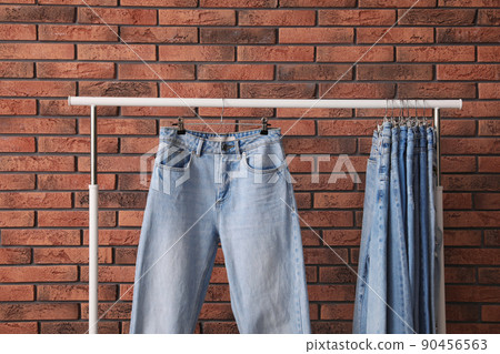 Rack with stylish jeans near brick wall, closeup Rack with stylish jeans near brick wall, closeup 90456563