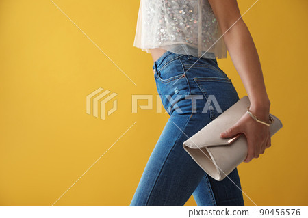 Woman in jeans with clutch purse on yellow background, closeup. Space for text 90456576