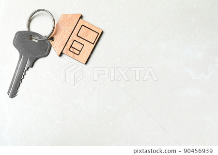 Key with trinket in shape of house on grey marble background, top view and space for text. Real estate agent services 90456939
