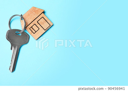 Key with trinket in shape of house on light blue background, top view and space for text. Real estate agent services 90456941