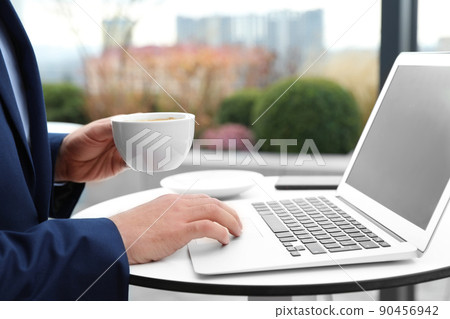 Businessman with laptop and coffee in outdoor cafe, closeup. Corporate blog 90456942