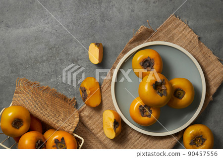 Top view of a light blue napkin of persimmon , green leaf in grey background for food advertising Top view of a light blue napkin of persimmon , green leaf in grey background for food advertising 90457556