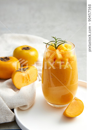 Front view of a tray with persimmon and persimmon frappe , green leaf in white curtain background for food advertising Front view of a tray with persimmon and persimmon frappe , green leaf in white curtain background for food advertising 90457568