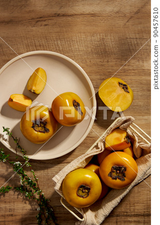 Top view of persimmon in white plate , flower , green leaf with grey background and blank space for advertising Top view of persimmon in white plate , flower , green leaf with grey background and blank space for advertising 90457610