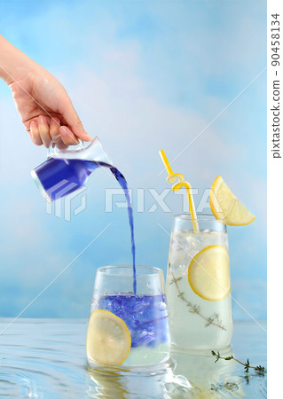 Woman's hand is pouring water from butterfly pea flower into a glass of lemon and honey tea. Butterfly pea or blue pea, Asia herb drink with lemon and honey.  90458134