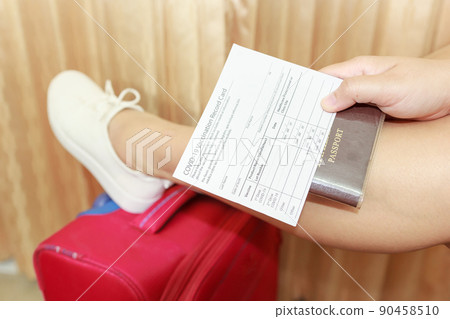 The legs of a tourist, wearing sneakers, lean on a suitcase. show relaxation with passport and vaccination records. Concept of safe travel from COVID-19. 90458510