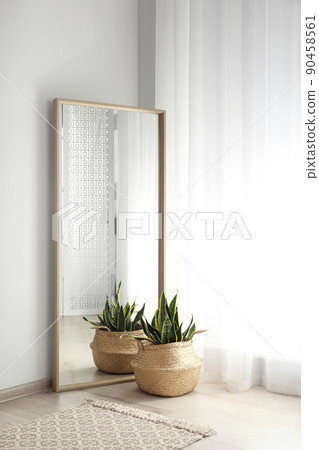 Large mirror with wooden frame near window in light room Large mirror with wooden frame near window in light room 90458561