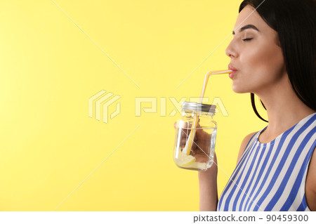 Beautiful young woman drinking tasty lemon water on yellow background, closeup. Space for text 90459300
