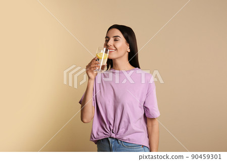 Beautiful young woman drinking tasty lemon water on beige background 90459301