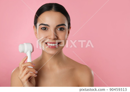 Young woman holding facial cleansing brush on pink background, space for text. Washing accessory 90459313