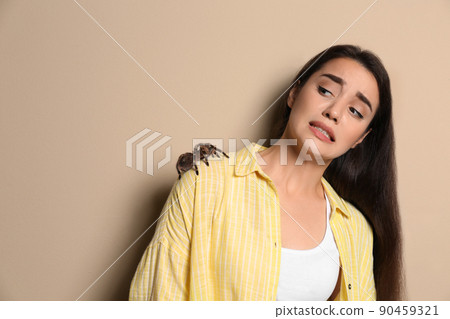 Scared young woman with tarantula on beige background. Arachnophobia (fear of spiders) 90459321