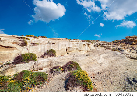 Summer landscape of rocks on Sarakiniko beach, Aegean sea, Milos island , Greece. No people, empty cliffs, sunshine, blue sky and clouds, some grass 90459352