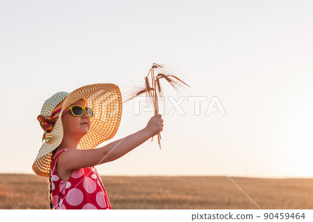 Child girl in straw hat dress in wheat field. Smiling kid in sunglasses sunset countryside. Cottagecore style aesthetic. 90459464