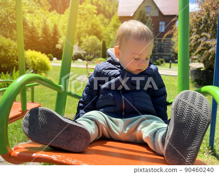 A cute boy of one and a half years rides on a swing. Backyard of the house. Children's entertainment. Selective focus 90460240