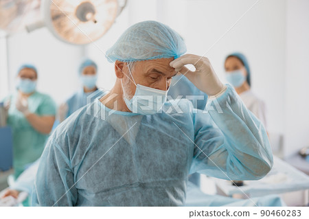 Close up of tired surgeon in mask standing in operating room after hard unsuccessful operation 90460283