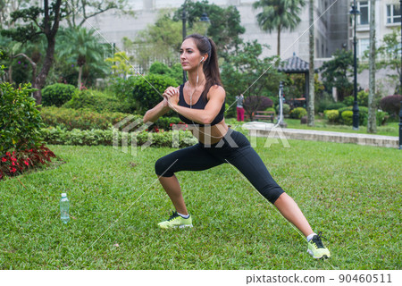 Pretty young fit woman doing stretching exercises in park. Fitness side lunges outdoors. 90460511