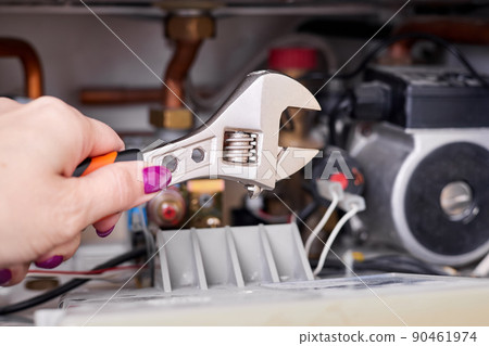 The girl is going to repair the gas boiler using an adjustable wrench 90461974