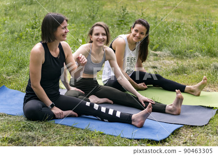 Young women useful stretching exercises on grass. Sports girls have fun doing fitness on yoga mats. 90463305