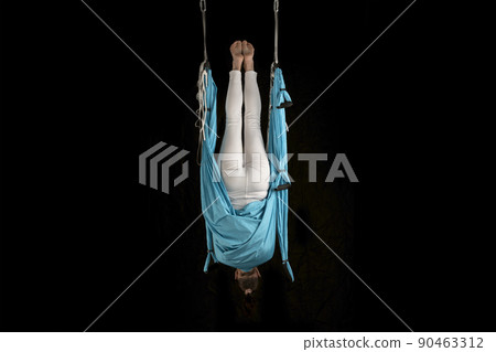 Young girl gymnast in sportswear doing stretching while hanging upside down. Aero fly yoga. Isolated on black background. Young girl gymnast in sportswear doing stretching while hanging upside down. Aero fly yoga. Isolated on black background. 90463312