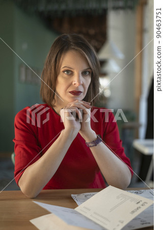 Stylish mature woman in red blouse sits at table in cafe. Portrait of business woman in cafeteria. Vertical frame. 90463751