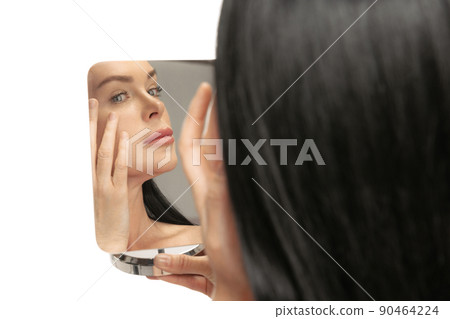 Close-up portrait of middle age, 44 years old beautiful woman with long black hair looks at her face in mirror. Beauty, age-related changes, face lifting and skin care concept. Close-up portrait of middle age, 44 years old beautiful woman with long black hair looks at her face in mirror. Beauty, age-related changes, face lifting and skin care concept. 90464224