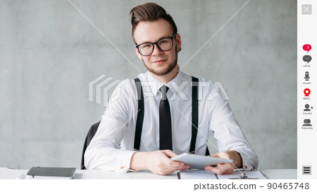 Web conference. Positive man. Screen mockup. Stylish smiling guy in spectacles sitting desk having online meeting in light room interior. Web conference. Positive man. Screen mockup. Stylish smiling guy in spectacles sitting desk having online meeting in light room interior. 90465748