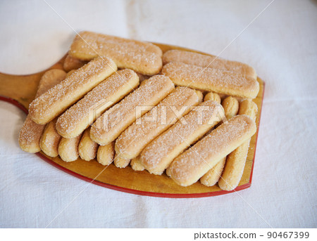 Top view of ladyfinger savoiardi biscuit cookies on a wooden cutting board on white tablecloth background. Close up 90467399