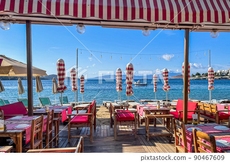 Beach umbrellas, sun loungers, tables and chairs on the shore of a calm blue sea bay in the early morning. Summer vacation and holiday destination concept 90467609