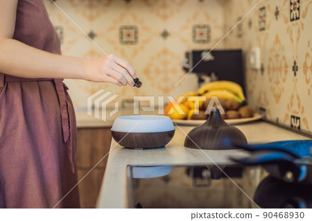 Woman adding essential oil to aroma diffuser on table Woman adding essential oil to aroma diffuser on table 90468930