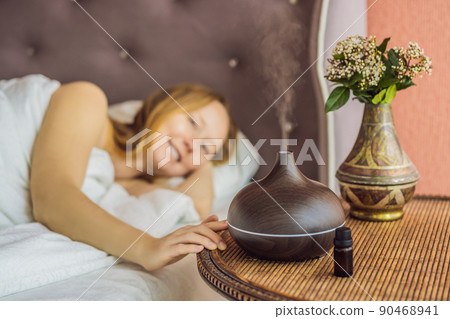 Aromatherapy Concept. Wooden Electric Ultrasonic Essential Oil Aroma Diffuser and Humidifier. Ultrasonic aroma diffuser for home. Woman resting at home Aromatherapy Concept. Wooden Electric Ultrasonic Essential Oil Aroma Diffuser and Humidifier. Ultrasonic aroma diffuser for home. Woman resting at home 90468941