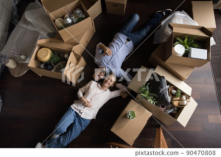 Overhead view homeowners couple lying on floor near cardboard boxes Overhead view homeowners couple lying on floor near cardboard boxes 90470808