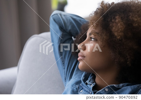 Pensive girl with natural curly hair resting on home couch 90470892