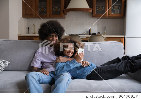 Cheerful Black couple using online app on smartphone at home 90470917