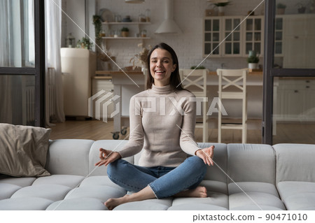 Happy cheerful young yogi woman practicing meditation on couch 90471010