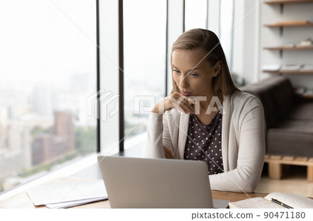 Thoughtful businesswoman working at laptop, reading text on screen Thoughtful businesswoman working at laptop, reading text on screen 90471180