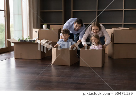 Siblings enjoy race seated inside boxes play with parents indoor Siblings enjoy race seated inside boxes play with parents indoor 90471189