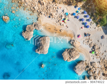 Aerial view of blue sea, beach with umbrellas, rocks in water 90474022
