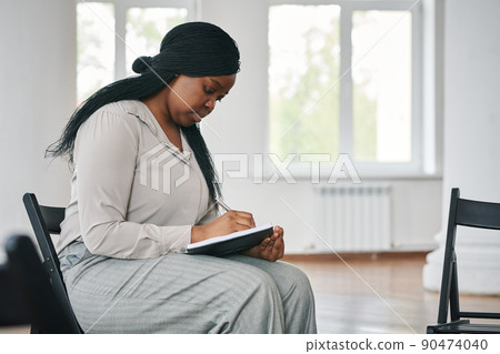 Young serious black woman making notes in notebook before or after session Young serious black woman making notes in notebook before or after session 90474040