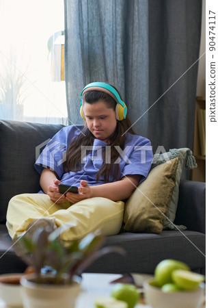 Young female with Down syndrome in headphones looking at smartphone screen Young female with Down syndrome in headphones looking at smartphone screen 90474117
