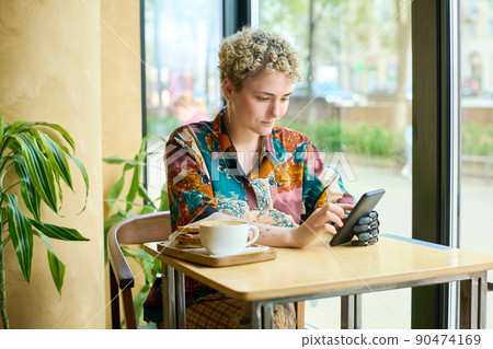 Young woman with physical impairment scrolling in smartphone in cafe Young woman with physical impairment scrolling in smartphone in cafe 90474169