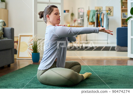Side view of girl with Down syndrome sitting on the floor with crossed legs Side view of girl with Down syndrome sitting on the floor with crossed legs 90474274