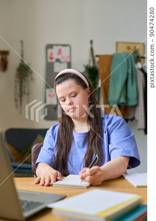 Female student with Down syndrome making notes during online lesson Female student with Down syndrome making notes during online lesson 90474280