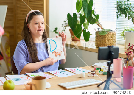 Young student with Down syndrome learning letters in front of smartphone camera Young student with Down syndrome learning letters in front of smartphone camera 90474298