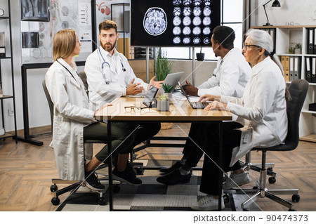 Doctors sitting at table and analyzing patient's MRI scan Doctors sitting at table and analyzing patient's MRI scan 90474373
