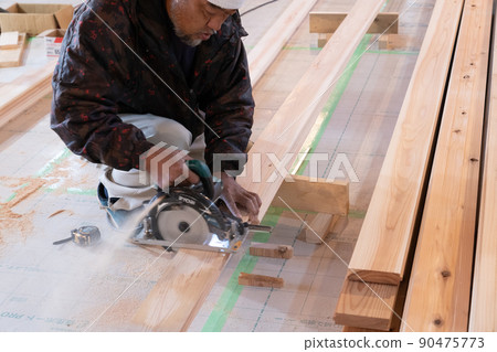 A carpenter who processes wood with an electric saw at the site of a wooden house A carpenter who processes wood with an electric saw at the site of a wooden house 90475773