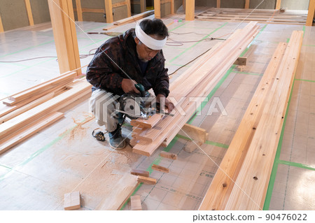 A carpenter who processes wood with an electric saw and a steel square at the site of a wooden house A carpenter who processes wood with an electric saw and a steel square at the site of a wooden house 90476022